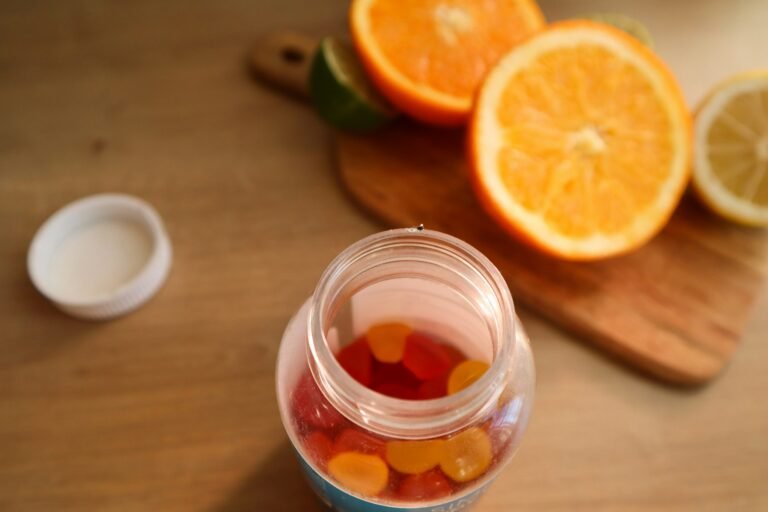 A glass jar of gummies next to sliced oranges on a wooden board